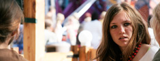 Wood-built cafeteria full of people. In the foreground, the face of a young dark-haired girl chatting with other people.