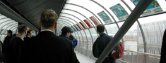 Glass tunnel with lots of people, seen from inside.